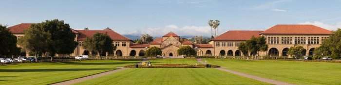 A panoramic of Stanford University, with red-roofed buildings beyond a lawn.
