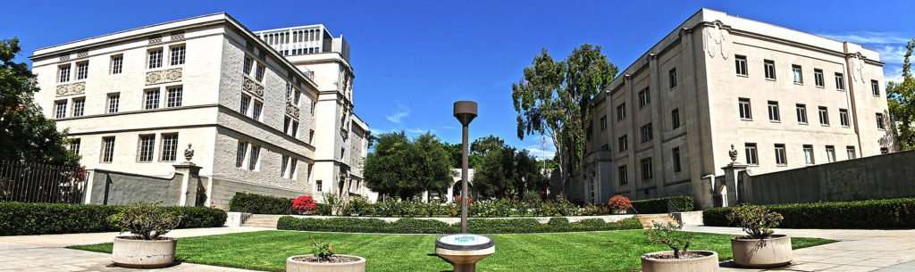 A well kept lawn is featured between two off-white buildings at the California Institute of Technology.