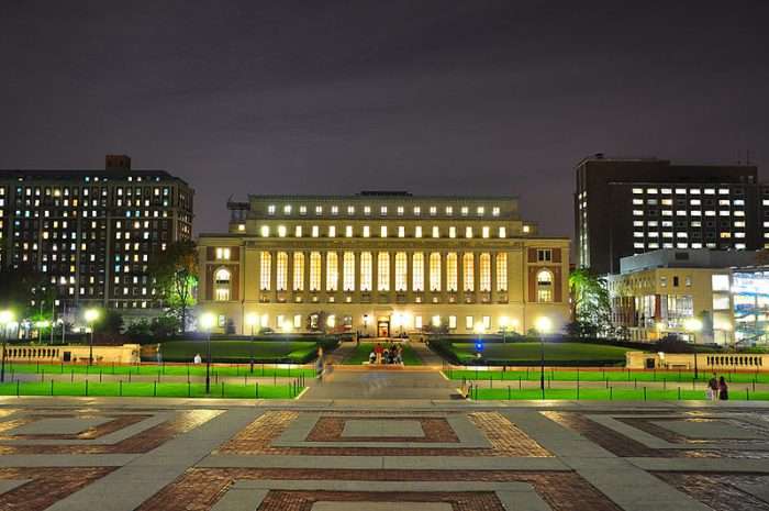 Columbia's library is lit up at night beyond a path.