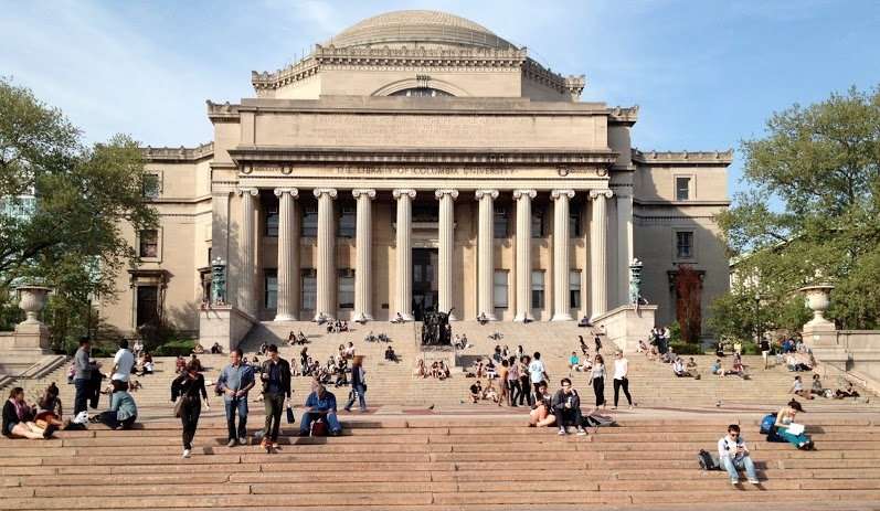 Columbia University's Low Library is pictured behind staircases laden with students relaxing and studying.