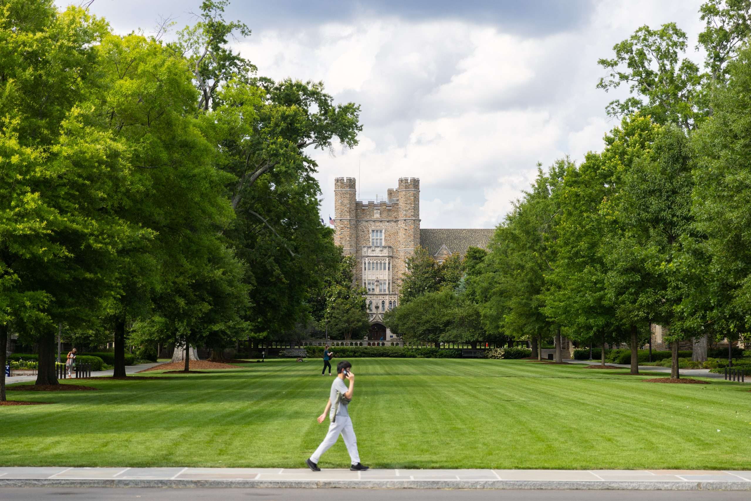 A person on his cell phone walks in front of Duke University's well-manicured lawn.
