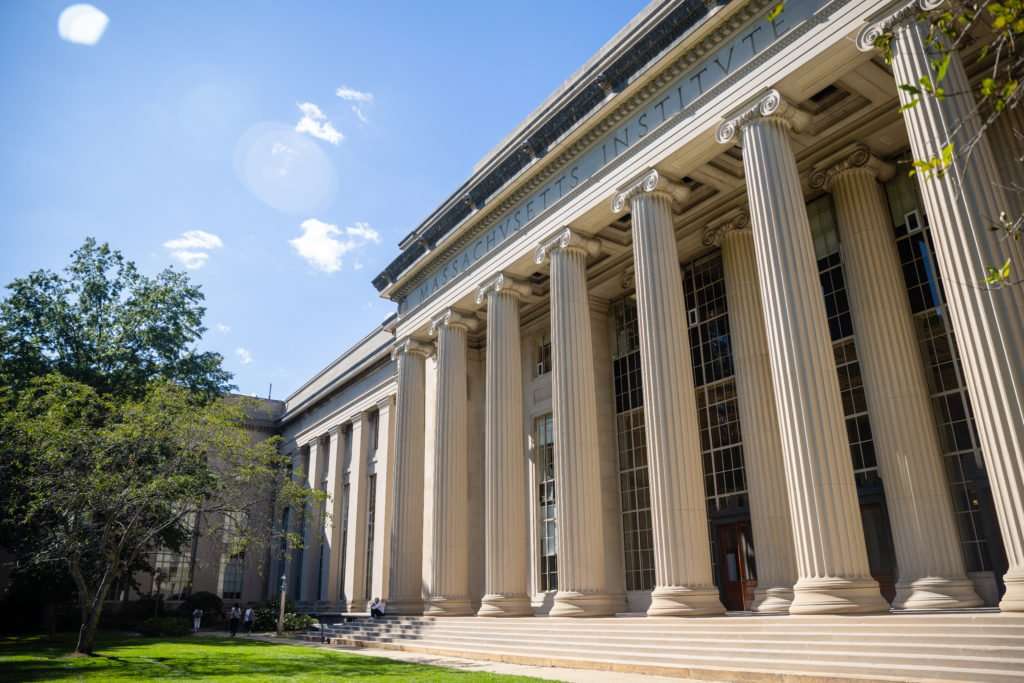 Beyond a lawn, a beautiful columned building with steps leading to the front doors is featured at the Massachusetts Institute of Technology.