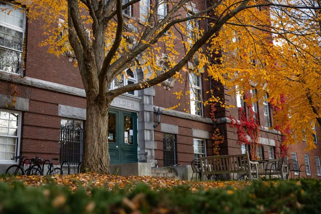 The red-bricked Wilder building sits beyond a tree with yellow leaves at Dartmouth College.
