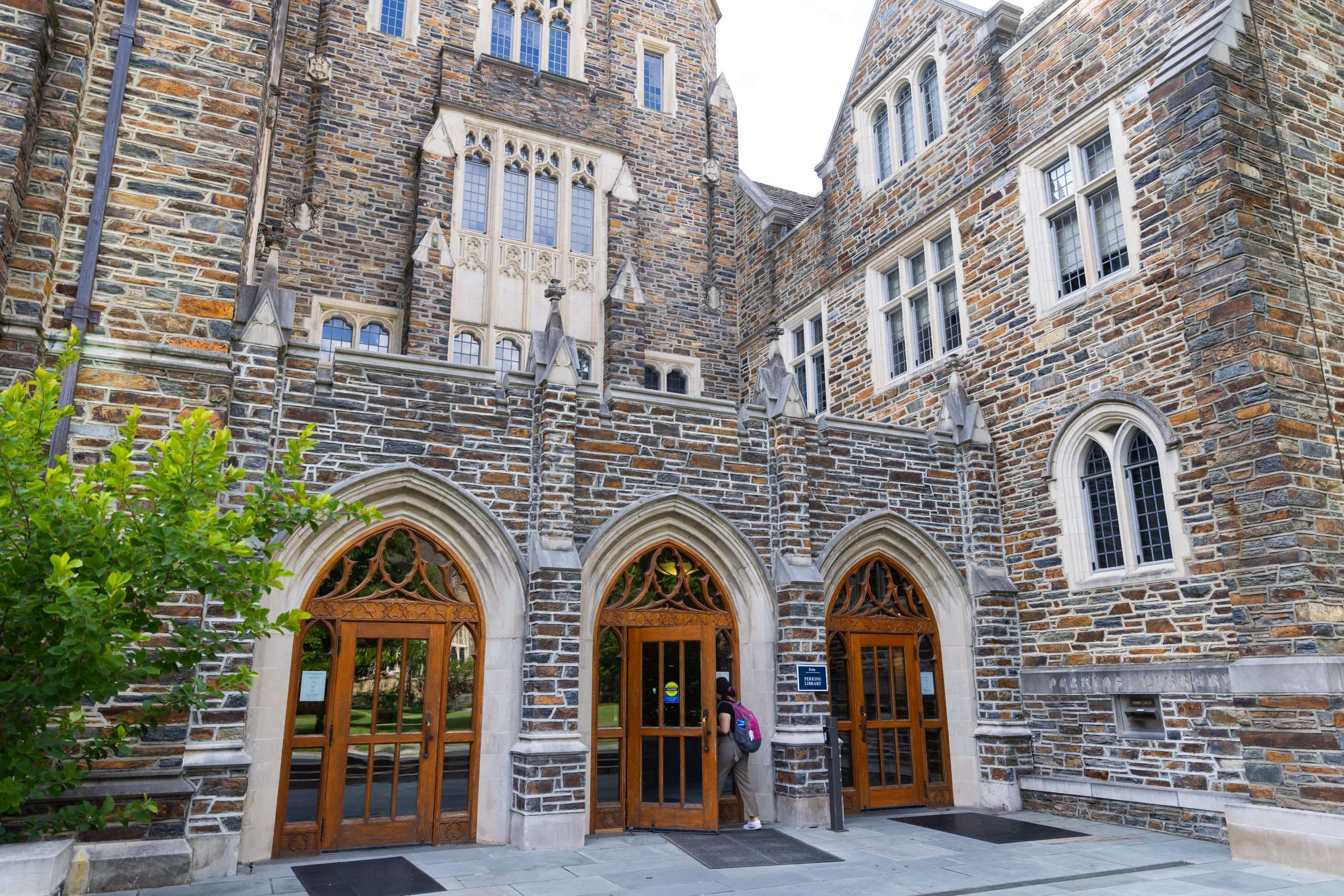 A person walks through the door to a gothic building on Duke University's campus.