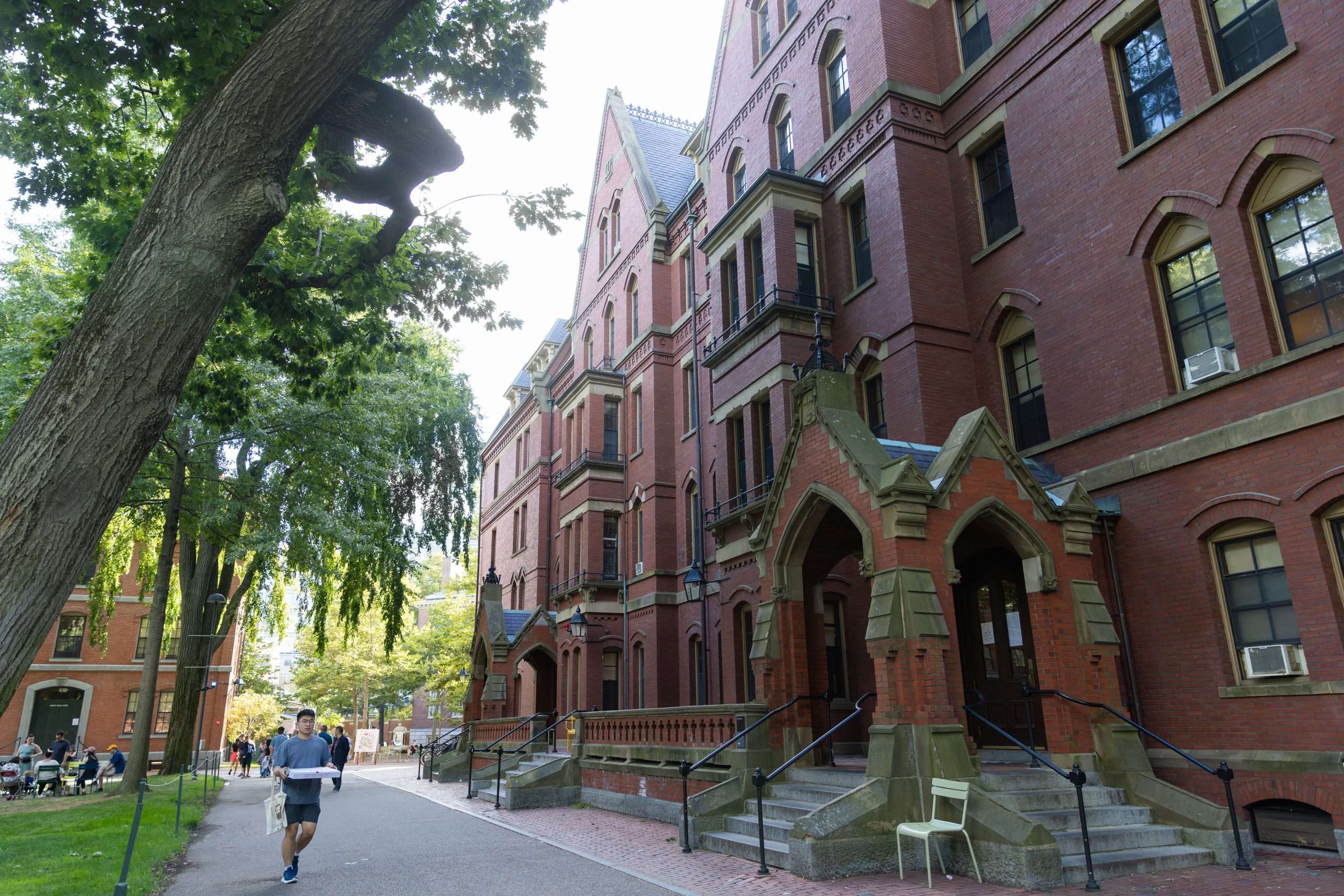 A student walks carrying a pizza pox in front of a castle-like building at Harvard University.